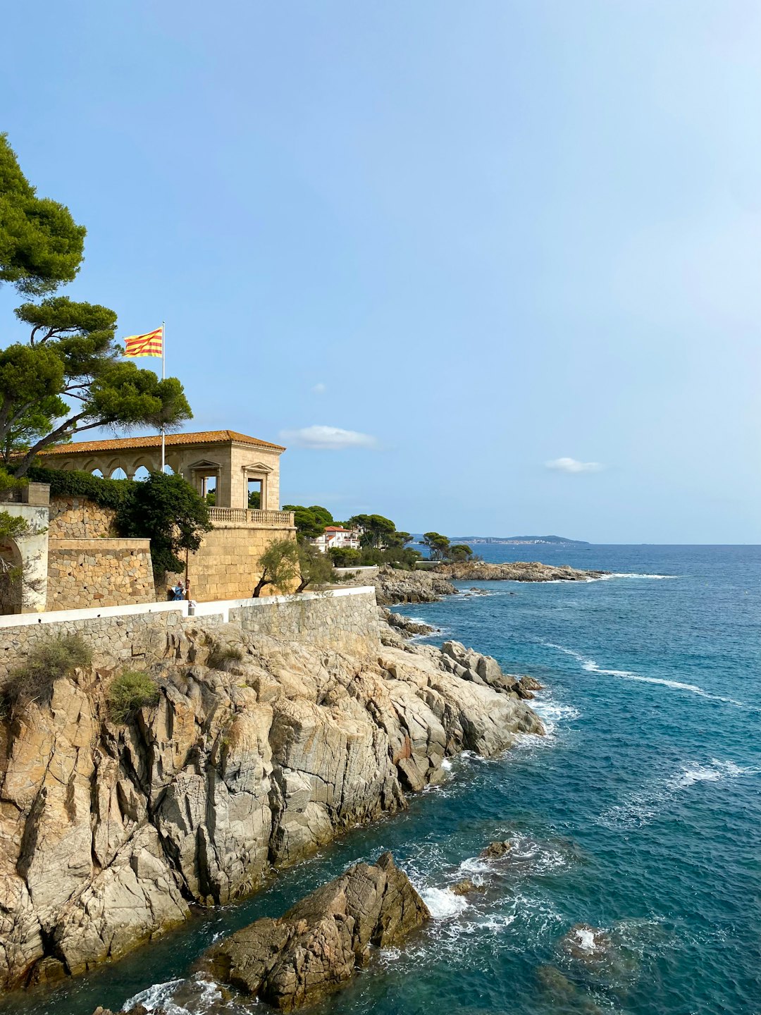 Mediterranean coastline with stone building on cliff and blue water.