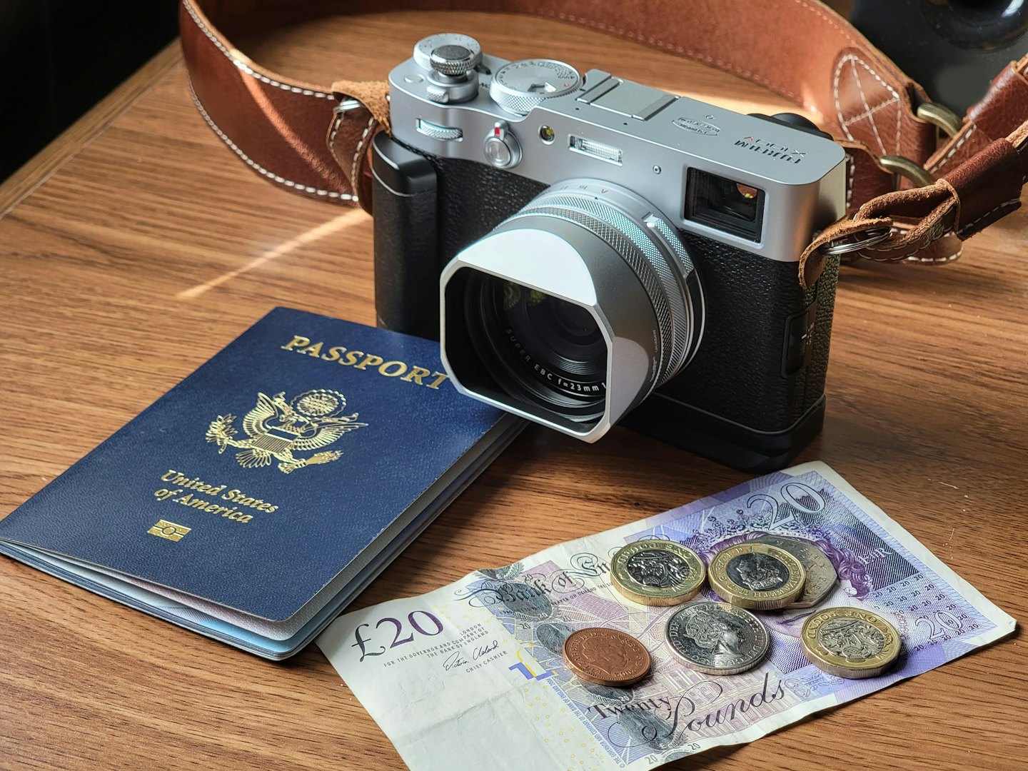 Travel essentials including a passport, currency, and camera on wood.
