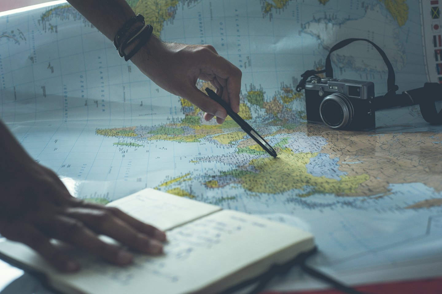 Hands planning a journey with a pen on a world map.