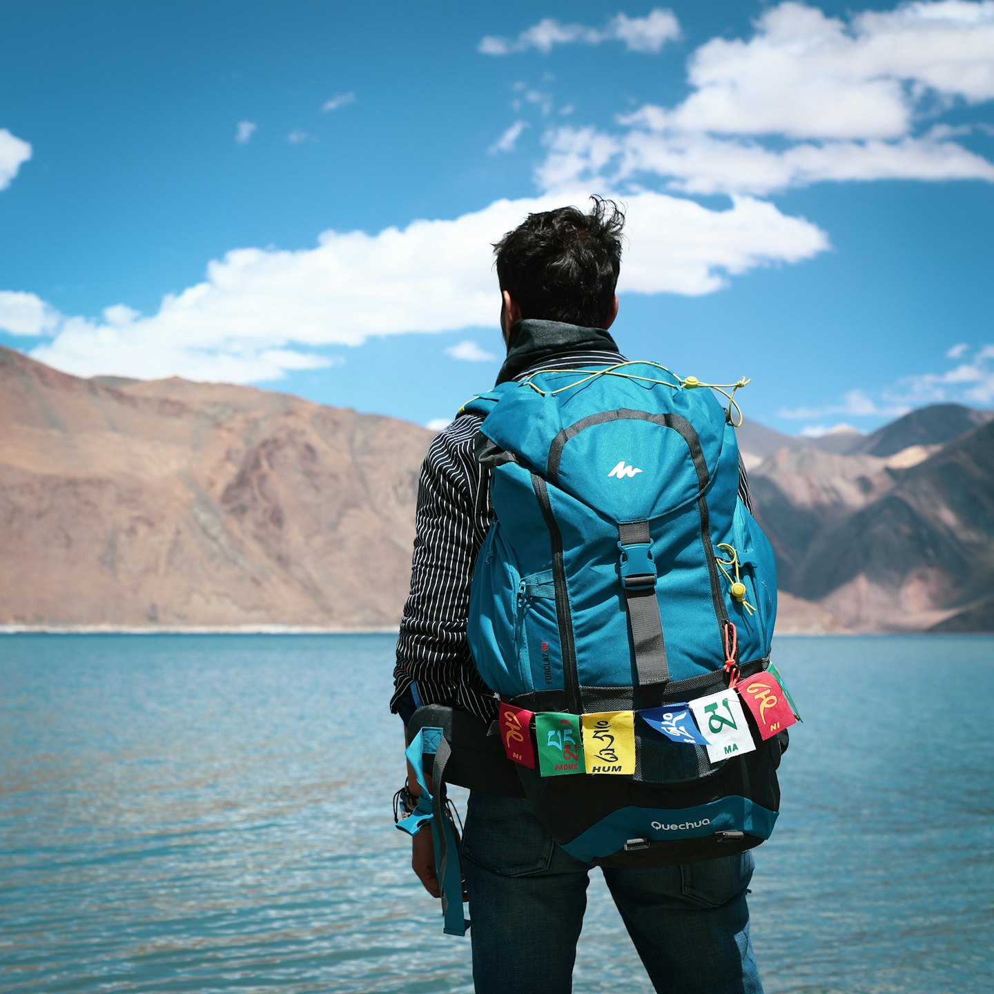 Hiker with a backpack looks out over a mountain lake.