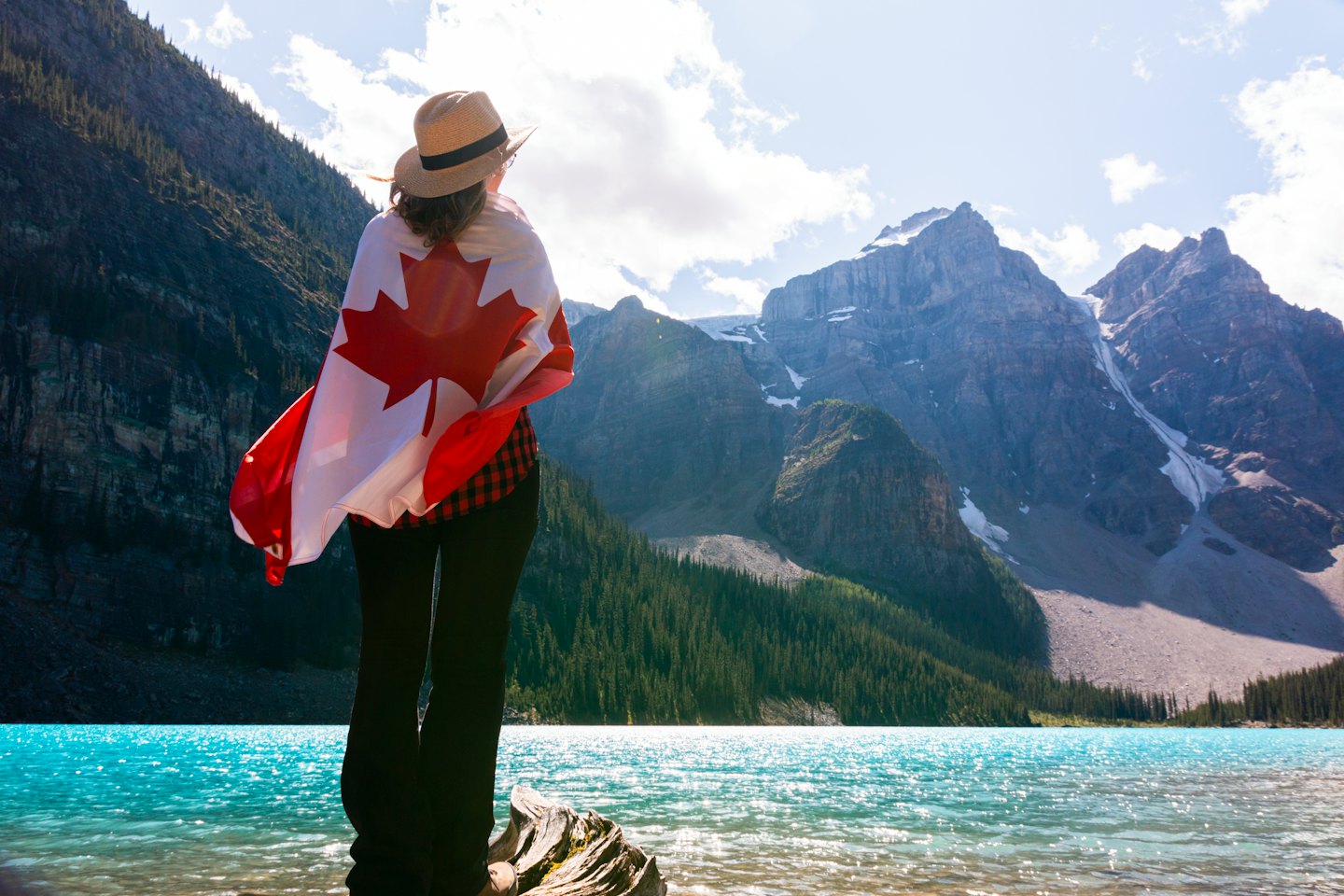 Person wrapped in a Canadian flag looks at mountain scenery.