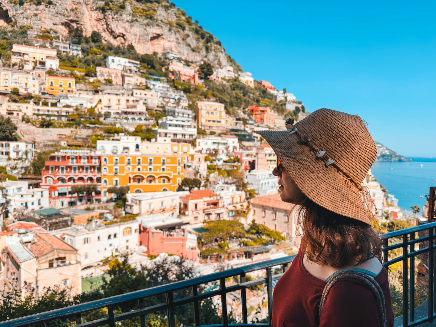 Traveler in a seashell hat overlooks a coastal hillside town.
